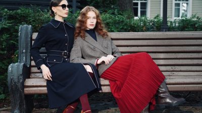 Two women in stylish fall outfits seated on a park bench, exuding elegance and sophistication.