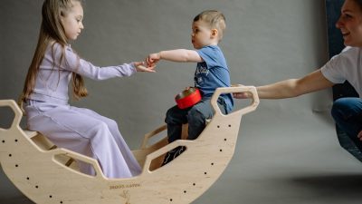 Young children play joyfully on a wooden rocker with a parent assisting in a studio setting.